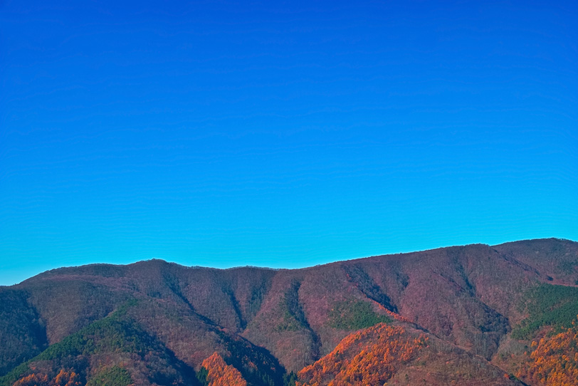 透き通った青い空と紅葉ある山裾の写真画像