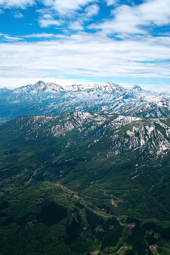 緑の山麓に残雪の山頂が雄大な春の山地の写真画像