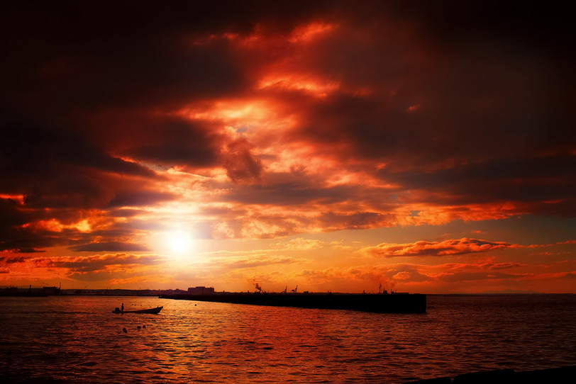 夕焼けの港と沖に向かう舟の写真画像