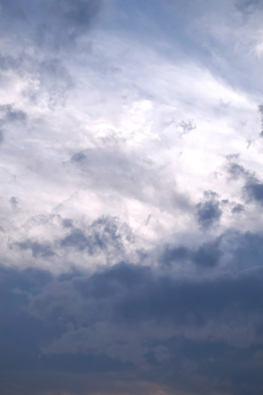 空に紺鼠色の雲と光に踊る断雲の写真画像