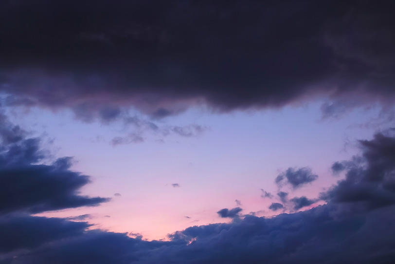 黒雲が囲む淡い夕焼けの写真画像