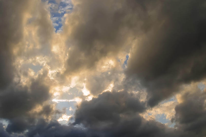 黒い畝雲から溢れる夕焼けの光の写真画像