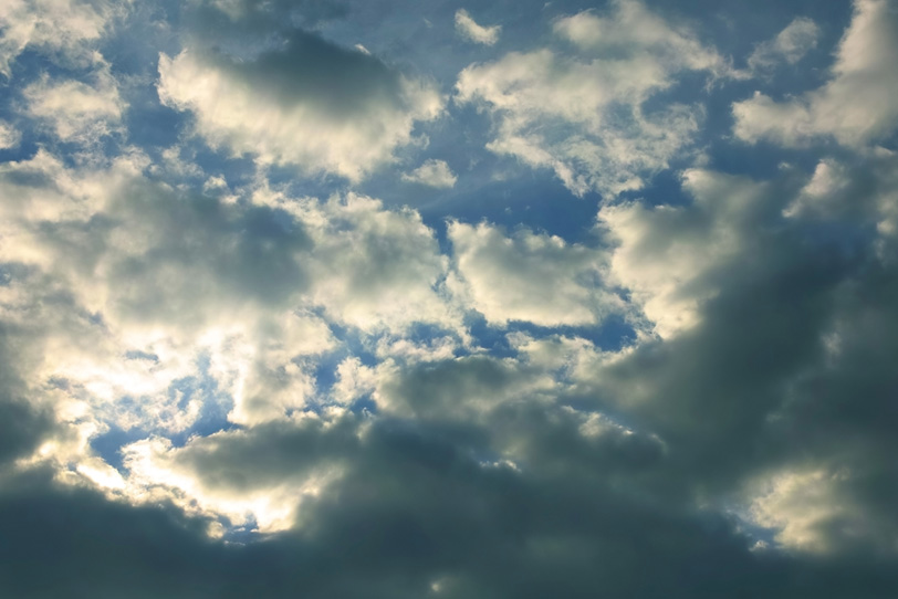 傾く陽に輝く雲と黒い青空の写真画像