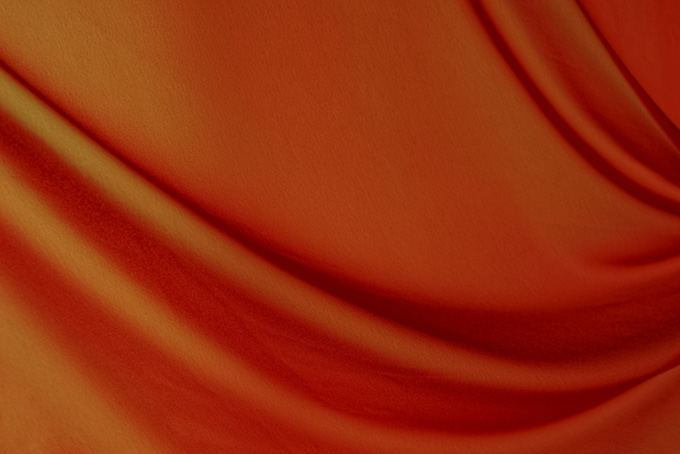豊かなドレープのあるオレンジ色の布の画像（布 ドレープの背景フリー画像）