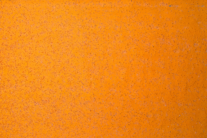 オレンジ色に塗装された鉄板に細かい錆が浮き出る（金属 素材の背景フリー画像）