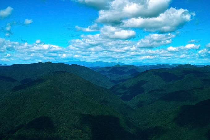 木々が生い茂る山脈に疎らに落ちる雲の影（山の背景フリー画像）