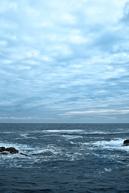 薄曇りの空と岩に砕ける波（海 風景の背景フリー画像）