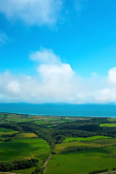 緑の丘の向こうの海辺の写真素材（背景 画像 海の背景フリー画像）