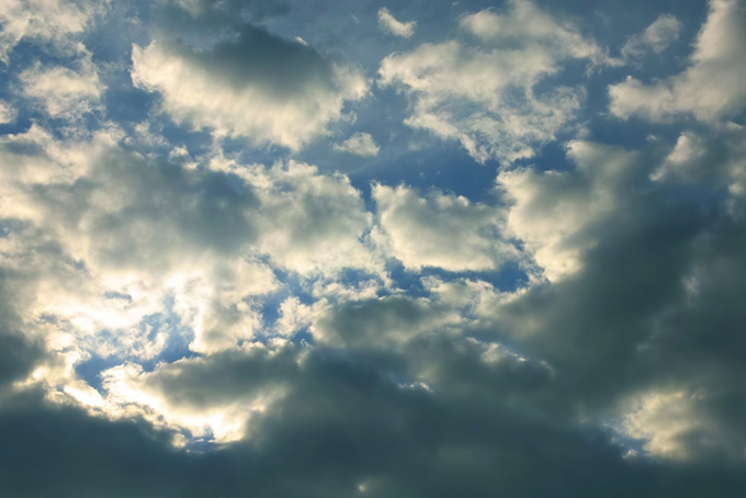 傾く陽に輝く雲と黒い青空（空 風景の背景フリー画像）